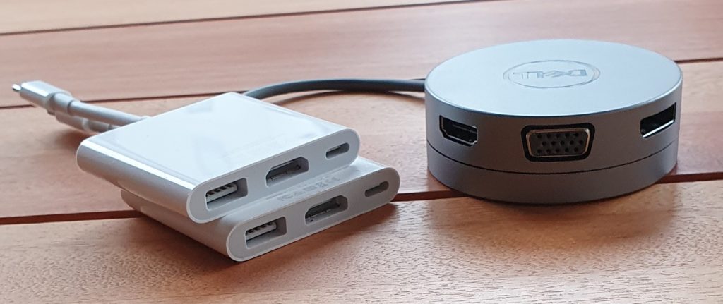 This image shows two Apple adapters sitting on top of each other (left). Both adapters did not correctly work. The Dell DA310, with HDMI and DisplayPort showing, sits on the right next to it.